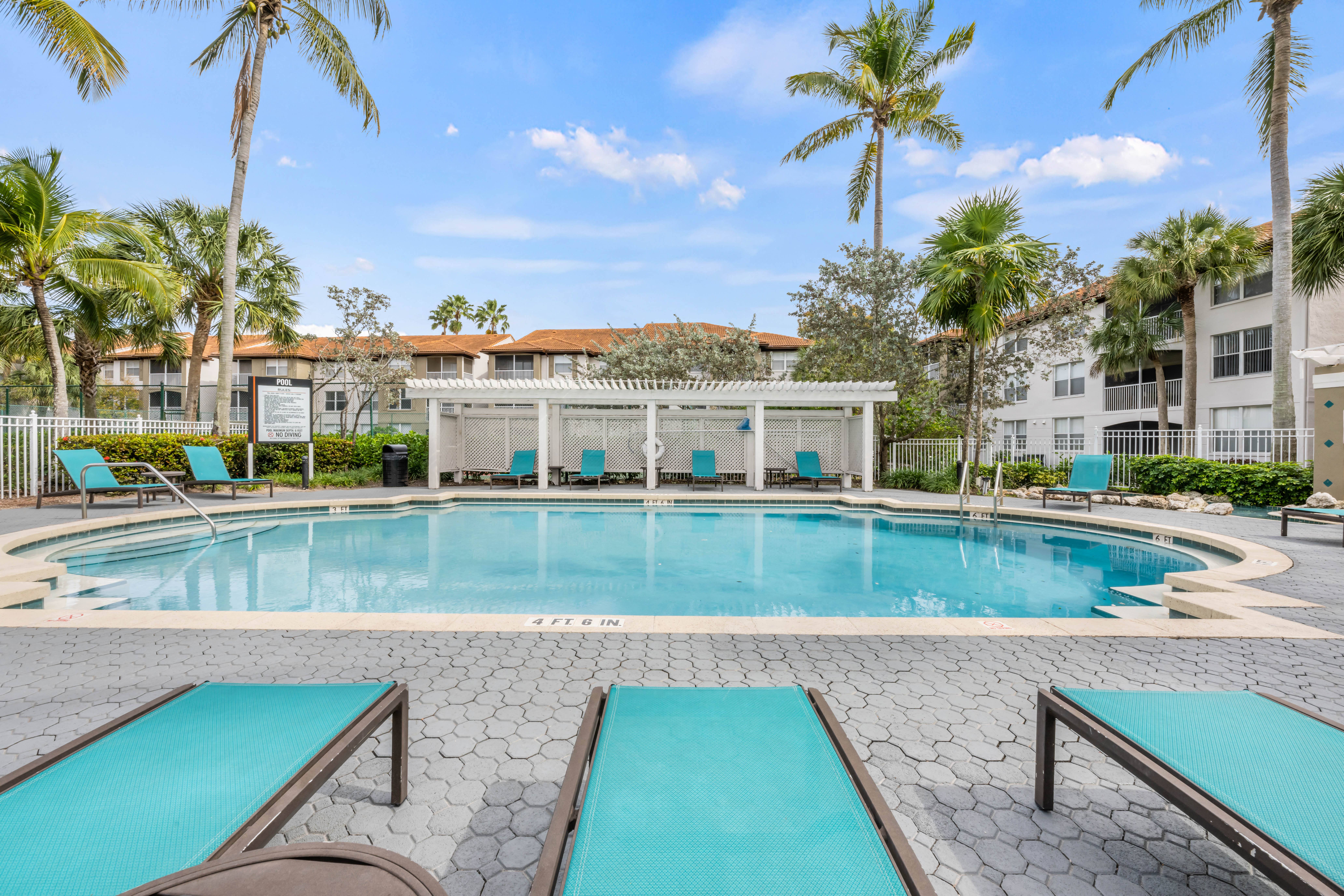 A pool surrounded by palm trees and lounge chairs.